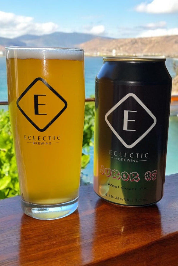 Pint glass and can of Eclectic Brewing beer on a wooden surface with a scenic background.